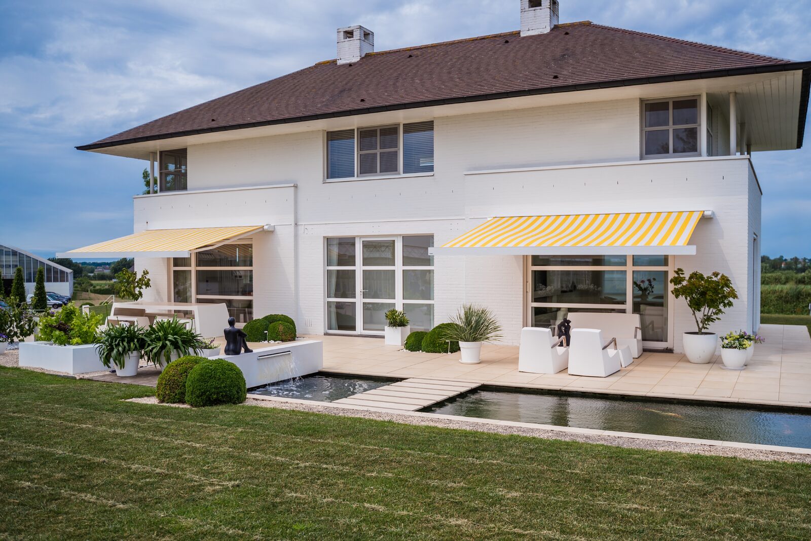 Twee afzonderlijke schermen van hetzelfde model, de markilux 970, aan de linker- en rechterzijde van het Terras, benadrukken de symmetrische architectuur van de woning nog meer.